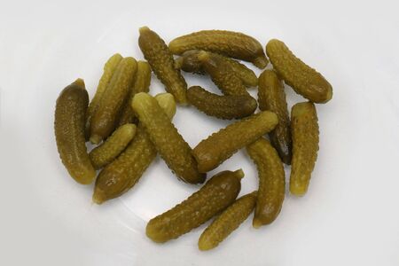 Mini pickled cucumbers preserved in brine on a white plateの写真素材