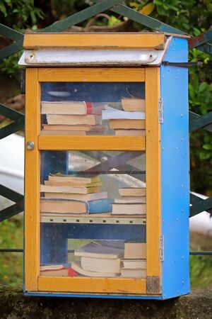 Large pile of second hand books on shelves inside metal box