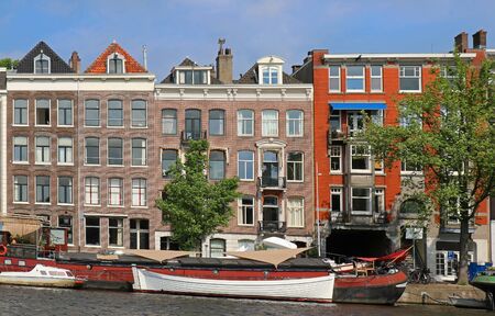 Retro residential houses on Amsterdam canal water and boats in frontの写真素材