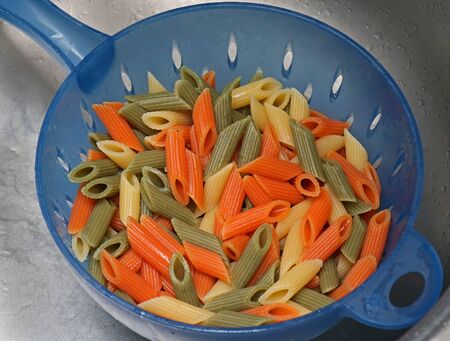 Colorful cooked penne pasta draining inside plastic strainerの写真素材