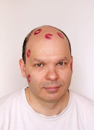 Red lipstick kisses marks on young man with bold headの写真素材