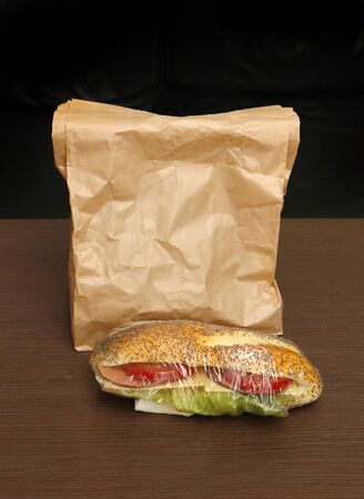 Healthy sandwich with tomato and lettuce inside bun next to paper bagの写真素材