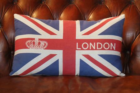Textile decorative pillow with Union Jack UK flag and London on it on brown leather sofaの写真素材