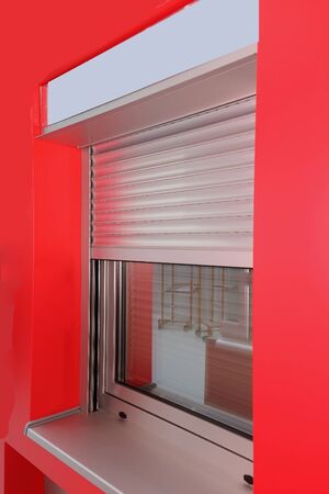 Half closed metal shutters on modern window exterior with red facade wallの写真素材