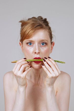 Young woman holding raw asparagus between her red lipsの写真素材