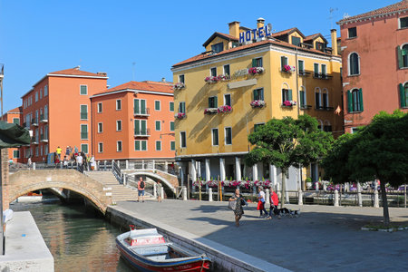 Venice, Italy - June 16, 2019: Tourists walking around Venice canals surrounded by ancient architecture colorful facade houses and crossing small bridge enjoying warm summer day.のeditorial素材