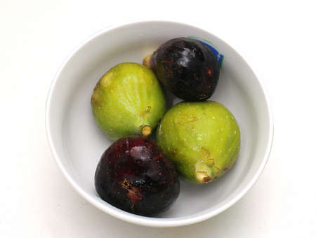 Raw organic green and purple figs fruits pile inside ceramic bowl on white backgroundの写真素材