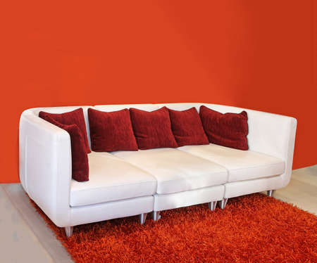 Modern white leather sofa inside interior with red wall and carpetの写真素材
