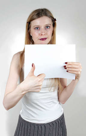 Young woman holding thumb up and blank paper in another handの写真素材