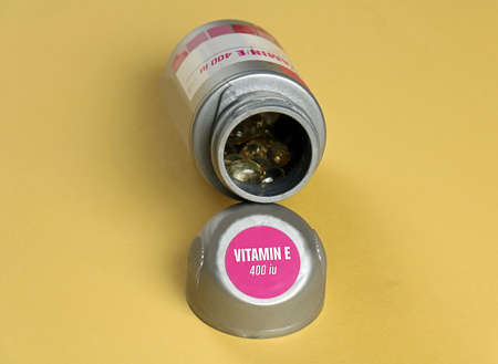 Vitamin E food supplement gel pills inside open container on yellow backgroundの写真素材