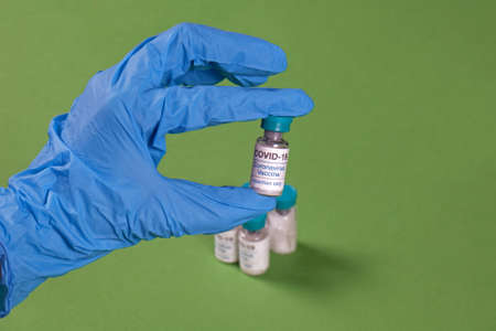 Hand in latex glove holding coronavirus vaccine inside medical centreの写真素材