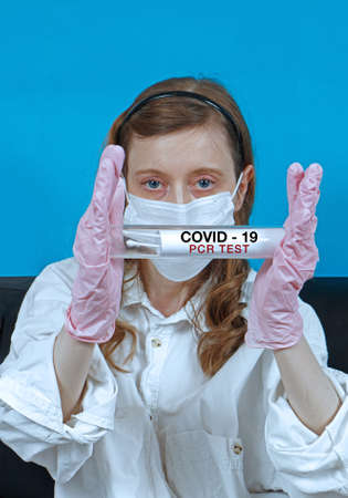 Young nurse wearing protective face mask and gloves holding swabs of COVID-19 pcr test samples inside tubeの写真素材