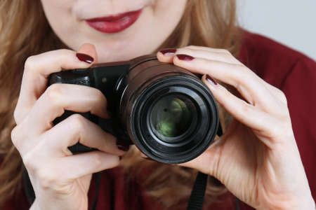 Woman photographer holding small digital camera to take pictures for various projects shot behind lensの写真素材