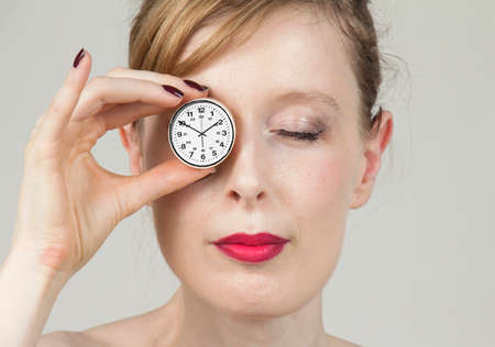 Young woman portrait with one eye closed and another with clock telling timeの写真素材