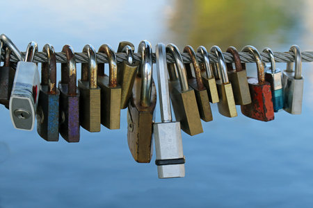 Old rusty metal padlocks hanging on string above riverの写真素材