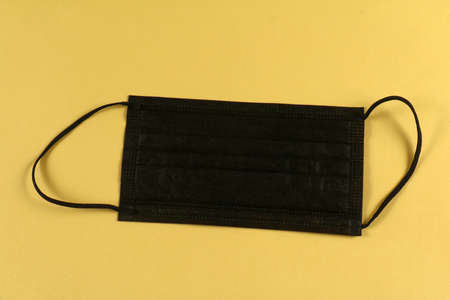 Black disposable face mask with 3 layers fabric isolated on yellow backgroundの写真素材