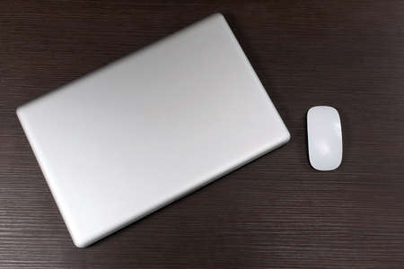 Modern closed laptop computer with wireless mouse on wooden table