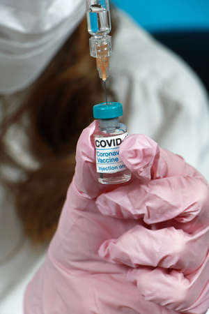 Nurse with latex glove and face mask protection loading syringe with covid-19 vaccine before injecting it into patient armの写真素材