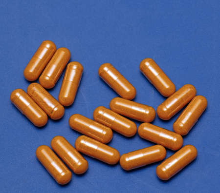 Big pile of turmeric dietary supplement capsules on blue backgroundの写真素材