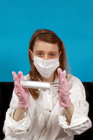 Young nurse wearing protective face mask and gloves holding test tube in hospitalの写真素材