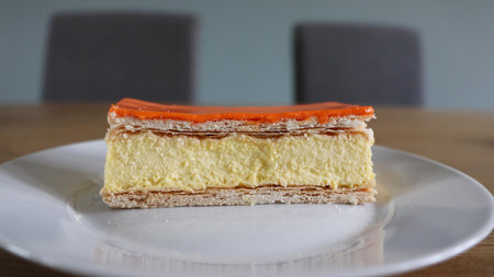 Orange cake on a white plate on a wooden table in a cafe, close up shot, Tompoes, tompouce, typical dutch cake, queensday, Koningsdag, puff pastry and pastry creamの写真素材