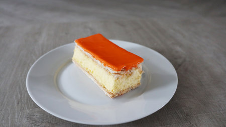 orange cake on white plate on wooden table, soft focus background, Tompoes, tompouce, typical dutch cake, queensday, kingsday, puff pastry and pastry creamの写真素材