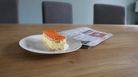 A piece of cake on a plate with newspaper in the background, Tompoes, tompouce, typical dutch cake, queensday, kingsday, puff pastry and pastry creamの写真素材