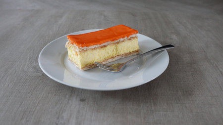 Piece of cake with orange cream on a white plate with a spoon, Tompoes, tompouce, typical dutch cake, queensday, kingsday, puff pastry and pastry creamの写真素材