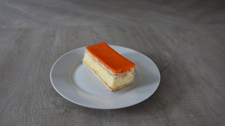 Orange cake on a white plate on a wooden table, selective focus, Tompoes, tompouce, typical dutch cake, queensday, kingsday, puff pastry and pastry creamの写真素材
