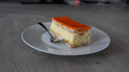 Orange cake on a white plate with a spoon on a wooden table, Tompoes, tompouce, typical dutch cake, queensday, kingsday, puff pastry and pastry creamの写真素材