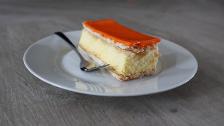 Orange cake on a white plate with a spoon on a wooden table, Tompoes, tompouce, typical dutch cake, queensday, kingsday, puff pastry and pastry creamの写真素材
