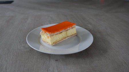 Orange cake in white plate on wooden table, shallow depth of field, Tompoes, tompouce, typical dutch...