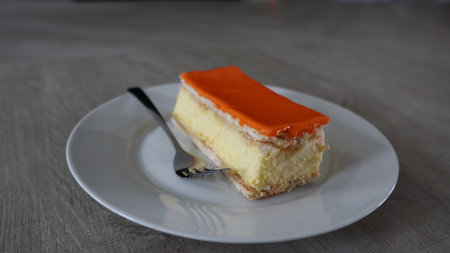 Orange cake on a white plate with a fork on the table, Tompoes, tompouce, typical dutch cake, queensday, kingsday, puff pastry and pastry creamの写真素材