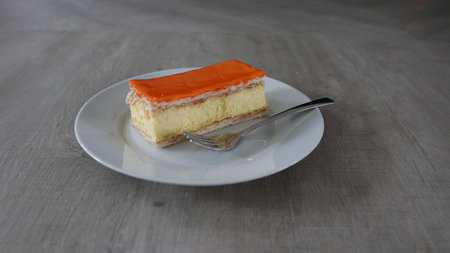 Piece of cake with orange jelly on a white plate with spoon, Tompoes, tompouce, typical dutch cake, queensday, kingsday, puff pastry and pastry creamの写真素材
