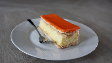 Orange cake on white plate with spoon on wooden table. Selective focus., Tompoes, tompouce, typical dutch cake, queensday, kingsday, puff pastry and pastry creamの写真素材