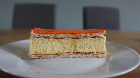 Orange cake on a white plate on a wooden table in a cafe, Tompoes, tompouce, typical dutch cake, queensday, kingsday, puff pastry and pastry creamの写真素材
