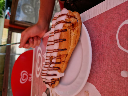 Hot dog with chocolate and cream on white plate in street cafe.の写真素材