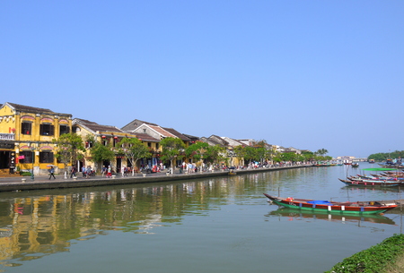 HOI AN, VIETNAM - 19TH MARCH 2018: Beautiful day in Hoi An ancient town with view of local people, boats, yellow houses by the river, and touristsのeditorial素材