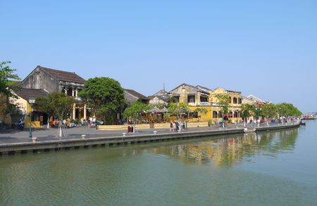 HOI AN, VIETNAM - 19TH MARCH 2018: Beautiful day in Hoi An ancient town with view of local people, boats, yellow houses by the river, and touristsのeditorial素材