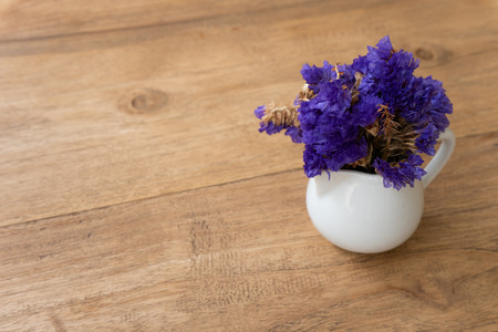Small violet flower in a white cup on a wooden tablein vintage background