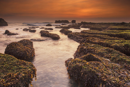 Sunset as seen from Mengening Beach, Bali,Indonesia. Mossy rocks in the foreground. Vibrant Colour.
