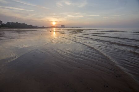 A fiery sunset on a Malaysia  coastal beach in the Asia. Waves splash against the colorful rocks and the sky is somewhat cloudy.の写真素材
