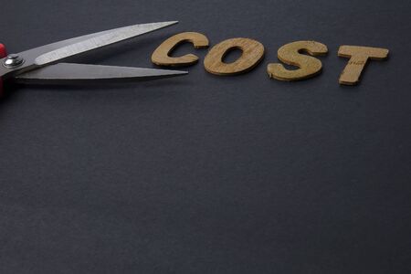 Pair of scissors cuts business expense word COST to save cost. Business concept and low light.の写真素材