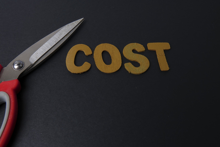 Pair of scissors cuts business expense word COST to save cost. Business concept and low light.の写真素材