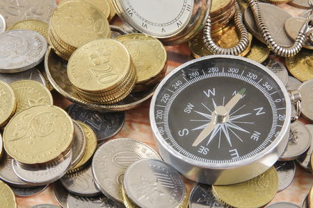 Antique clock,compass and pile of coins. Business direction and movement concept. Selective focus.