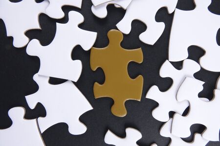 Gold puzzle stand out within white puzzles on black background.の写真素材