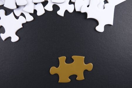 Gold puzzle stand out within white puzzles on black background.の写真素材