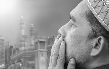 Adult man praying  wholeheartly over Mecca construction site. Blurred background.の写真素材