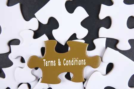 Fingers holding piece of blank jigsaw puzzle with word TERMS & CONDITIONSの写真素材