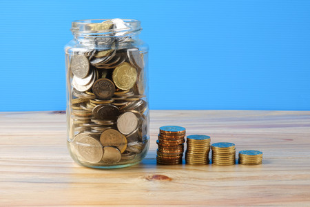 Mason jar with coins over blue back drop. Saving concept.